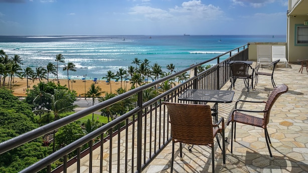 A balcony with wicker furniture overlooking a beach with palm trees and the ocean.