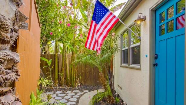 A garden pathway leading to a blue door, with an American flag hanging above.