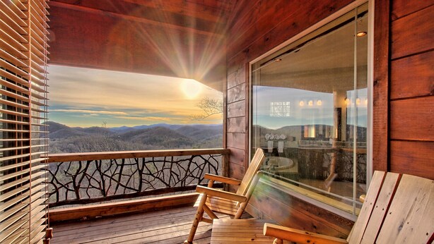Una terraza de madera con vistas a montañas, una silla de madera y un ventanal de vidrio.