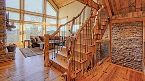 Un espacio habitable amplio con una escalera de madera, ventanas grandes y una pared de piedra.
