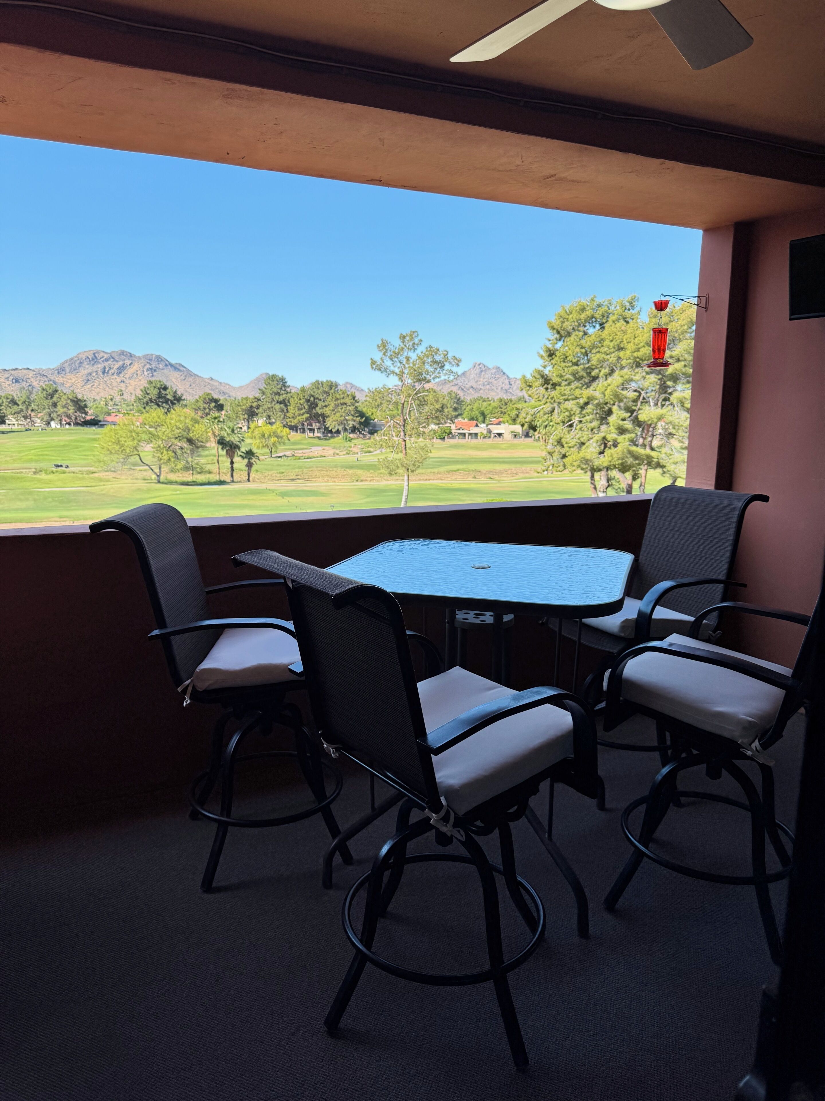 A balcony with a table and chairs, a ceiling fan, and a view of a golf course and mountains.