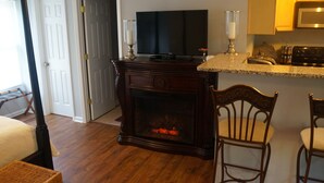 A living room with a fireplace, a television, and a kitchen area with a microwave.