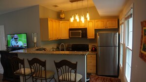 A kitchen with wooden cabinets, a microwave, a refrigerator, and a bar area with chairs.