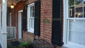 A brick building with black shutters, a white door, and a bench outside.