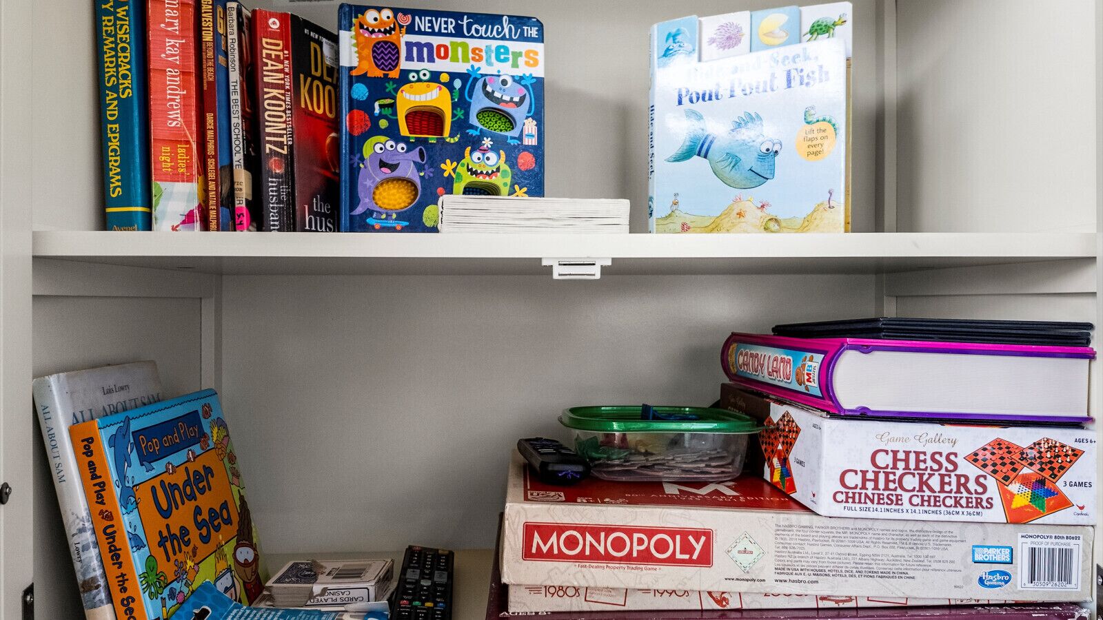 A shelf with various board games and books, including 'Never touch the monsters' and 'Pout Pout Fish'.