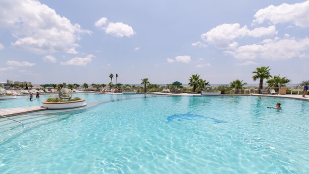 A large outdoor swimming pool with clear water, surrounded by palm trees and lounge chairs. - Rates just lowered.  Enjoy The WHITE BEACHES, LAZY RIVER, the CARIBE has it ALL (Orange Beach)