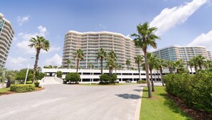 A large, multi-story hotel with a curved facade, surrounded by palm trees and well-maintained lawns. - Rates just lowered.  Enjoy The WHITE BEACHES, LAZY RIVER, the CARIBE has it ALL (Orange Beach)
