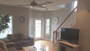 A living room with a grey sofa, a white coffee table, a TV on a wooden stand, and a staircase leading upstairs. - Best Location In LBI! Walk To Everything (Beach Haven)