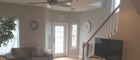 A living room with a grey sofa, a white coffee table, a TV on a wooden stand, and a staircase leading upstairs.