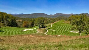 Ein Golfplatz mit gepflegten Fairways und Greens, umgeben von Bäumen und Bergen.