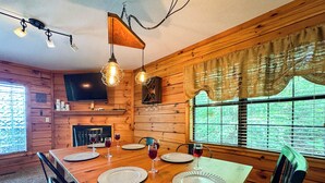 Ein Esszimmer mit Holzboden, einem großen Tisch für vier Personen, einem Kamin und einem an der Wand befestigten Fernseher.