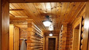 A wooden log cabin interior with a hallway leading to a door, a radiator, and a hanging light fixture.
