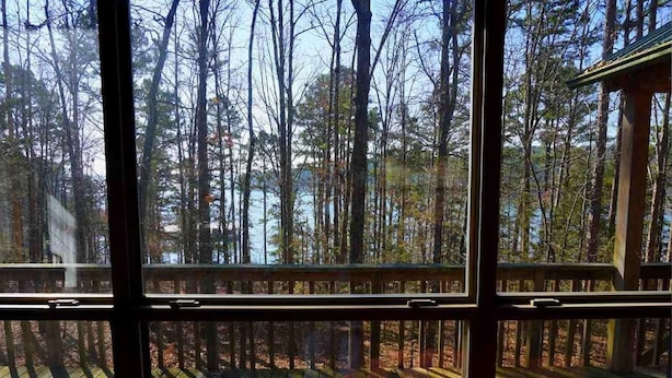 A view through large windows of a forested area with a wooden deck in the foreground.