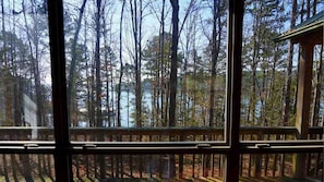A view through large windows of a forested area with a wooden deck in the foreground. - Spacious Lakefront Log Home Retreat (Higden)