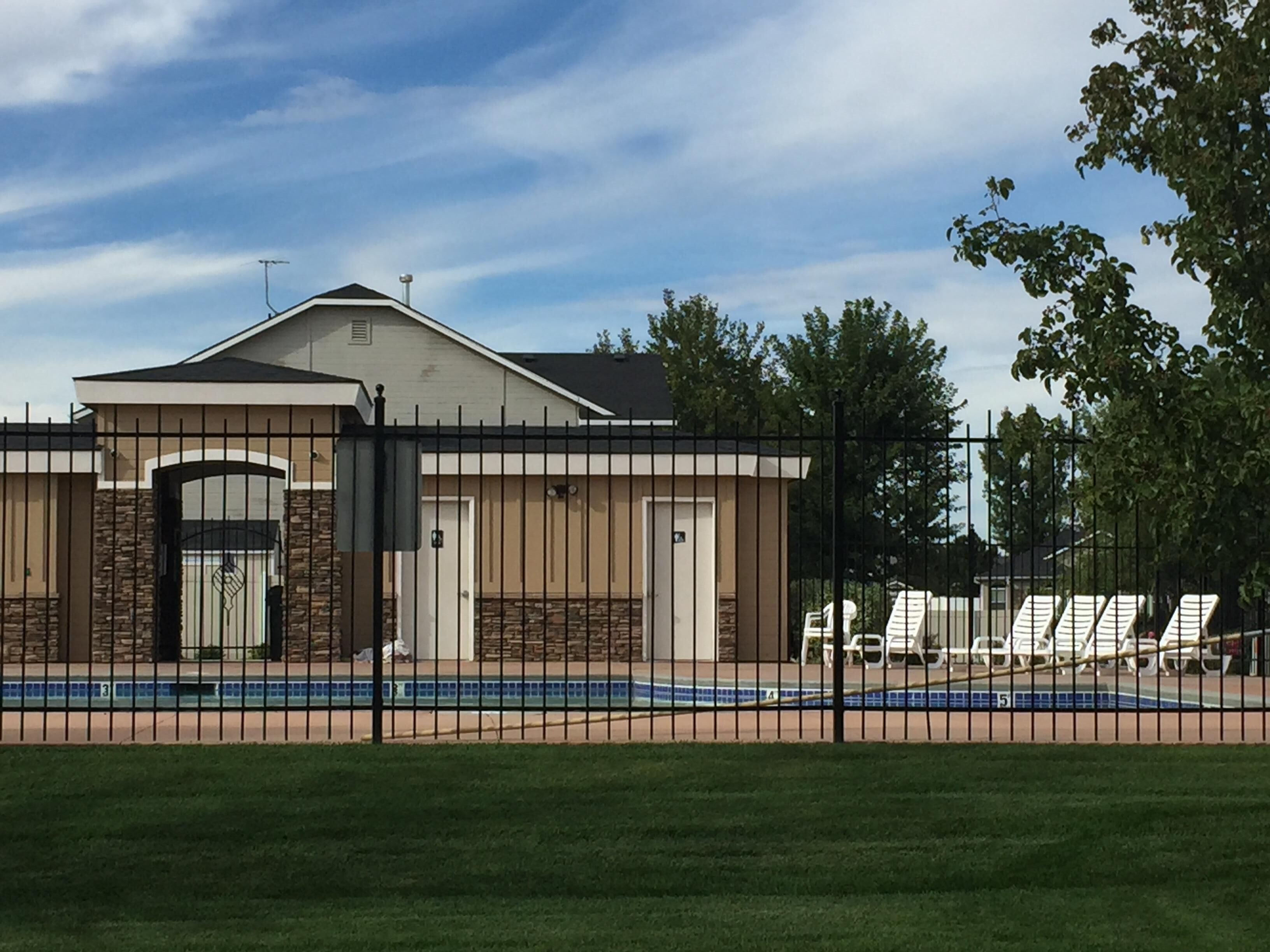 A building with a gated entrance, a swimming pool, and lounge chairs.