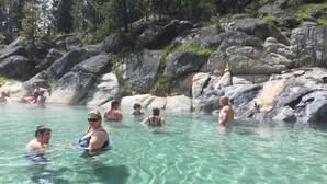 Une source d’eau chaude naturelle, aux eaux cristallines, entourée de grands rochers et d’arbres.