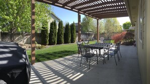 Une terrasse couverte avec une table et des chaises, un barbecue et une pelouse bien entretenue.