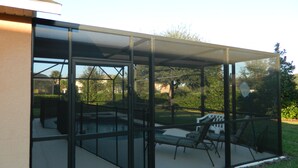 A covered outdoor area with a glass enclosure, a patio with a table and chairs, and a lawn. - Private Villa For Holiday Rental (Clermont)
