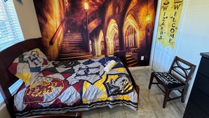 A bedroom with a large tapestry depicting a gothic staircase, a bed with a quilt featuring various logos, and a chair with a black cushion. - Private Villa For Holiday Rental (Clermont)