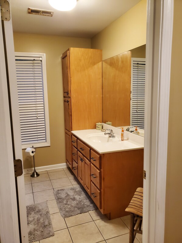 Un baño con tocador de madera, lavamanos con espejo e inodoro.