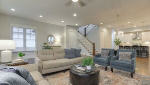 A spacious living room with a sofa, armchairs, a coffee table, and a staircase leading to a kitchen.