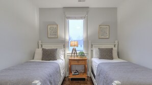 A bedroom with two beds, a nightstand with a lamp, and framed artwork on the walls.