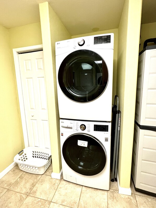 A stacked washer and dryer unit in a laundry room with a door, a laundry basket, and a refrigerator.