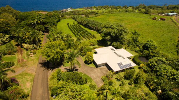 An aerial view of a property with a large green field, a building with solar panels, and a view of the ocean. - Garden Home at Botanical World Adventures 
Two Bedroom Three bathroom  (Hakalau)