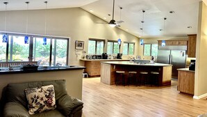 A spacious kitchen with a large island, wooden cabinets, and a view of the outdoors through multiple windows. - Garden Home at Botanical World Adventures 
Two Bedroom Three bathroom  (Hakalau)