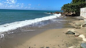 A beach with clear blue water, a sandy shore, and a rocky outcrop.