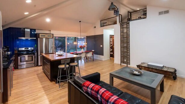 A spacious living area with a kitchen, a dining table, and a sofa with a plaid throw.