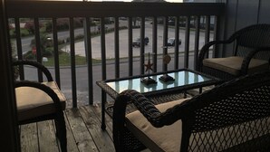 Un balcon avec des fauteuils en osier et une table en verre, donnant sur une rue animée par la circulation des voitures et bordée d’immeubles.