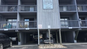 Un immeuble à plusieurs étages doté de balcons, une enseigne indiquant « Carolina Lake Beach Villas », et un espace de stationnement où se trouve un vélo.