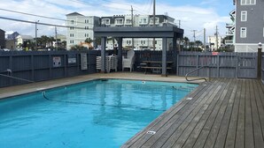 Une terrasse en bois avec une piscine, un espace salon couvert et une vue sur les immeubles résidentiels en arrière-plan.