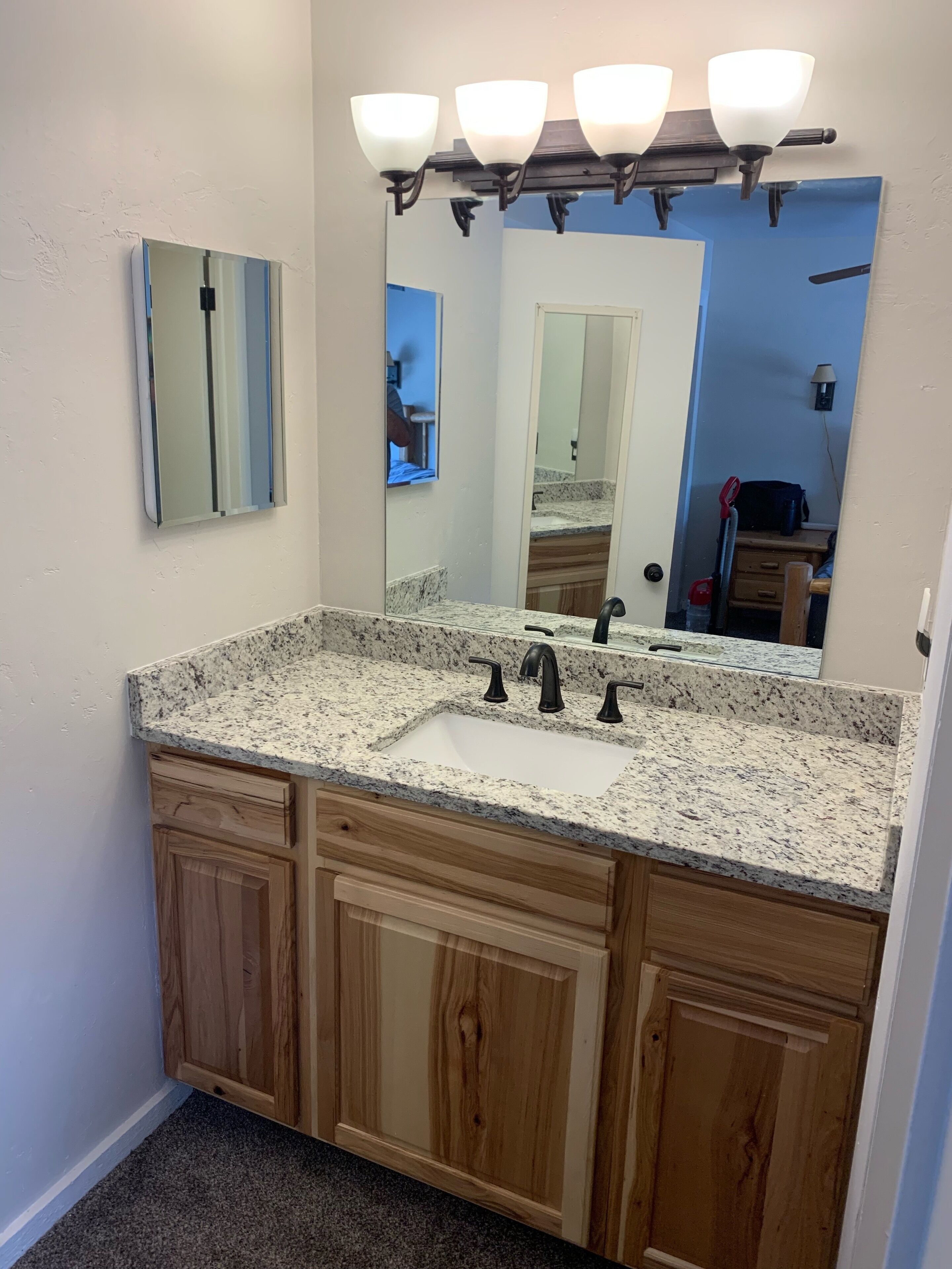 A bathroom with a granite countertop sink, wooden cabinets, a large mirror, and a light fixture above the mirror.