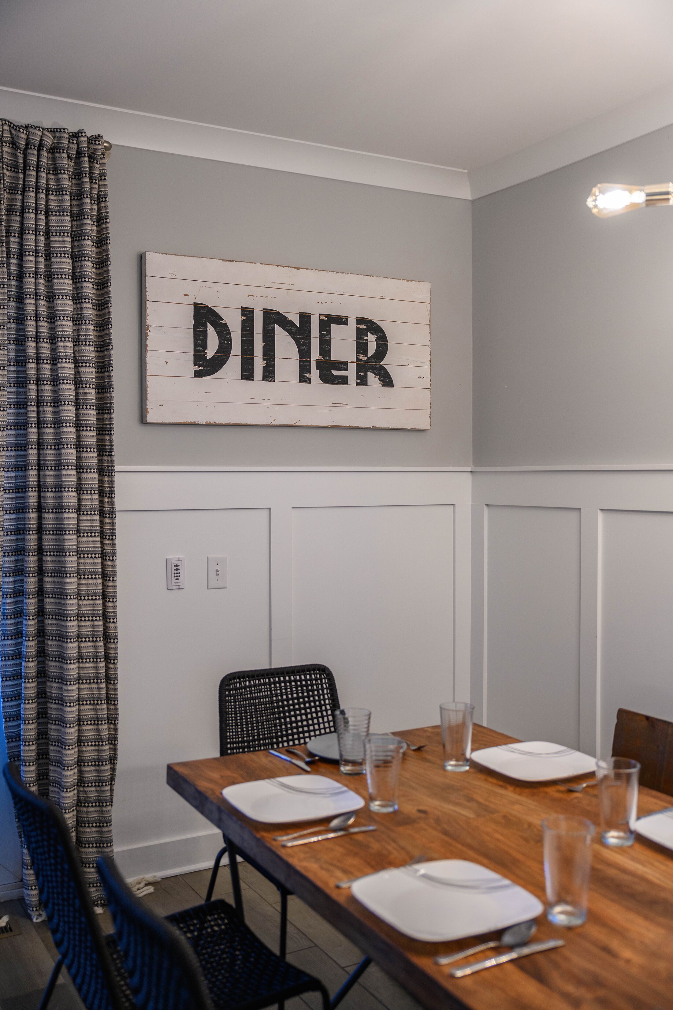 A dining area with a wooden table set for four, a sign above reading "DINER," and a black chair with a woven seat.