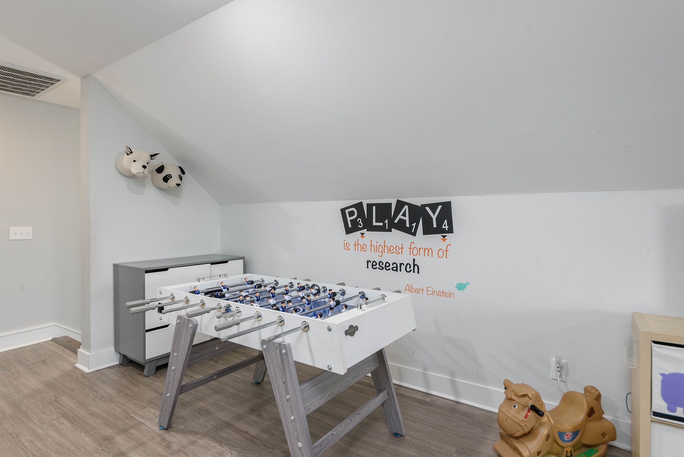 Une pièce avec une table de baby-foot, un canapé et un mur orné d’une citation inspirante.