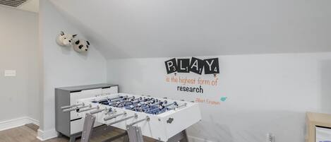Une pièce avec une table de baby-foot, un canapé et un mur orné d’une citation inspirante.
