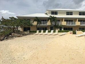 A beachfront hotel with a flat roof, multiple balconies, and sun loungers.