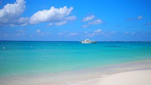 Uma praia com águas turquesa cristalinas, um barco ao longe e uma faixa de areia.