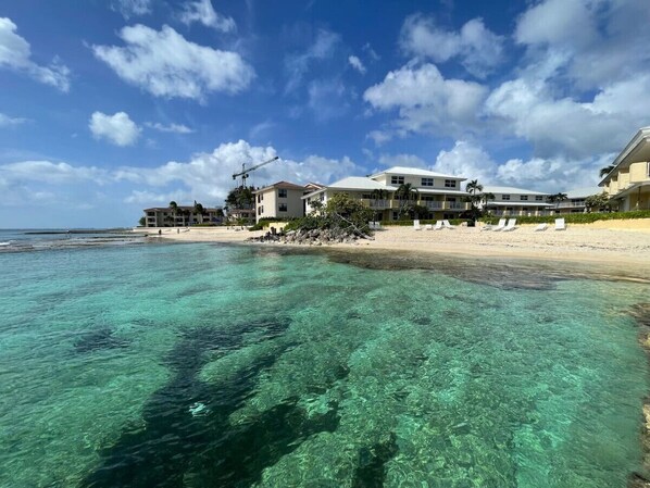 Un hotel frente a la playa con aguas cristalinas, una playa arenosa y cielo despejado.