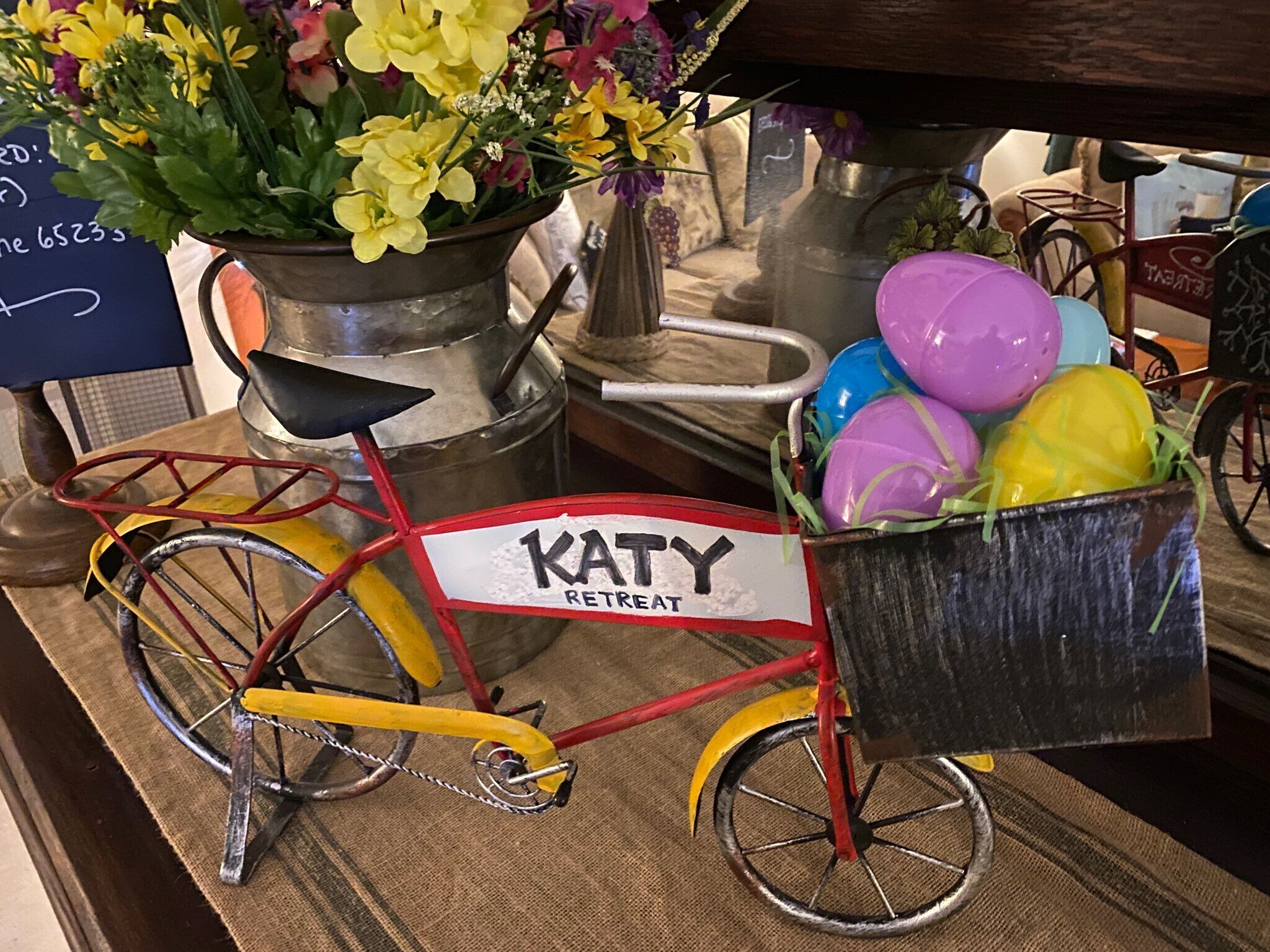 A bicycle with a basket labeled "KATY RETREAT" and a pot of flowers.