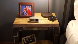 Ett sängbord med en lampa, ett inramat foto, en klocka och en skylt som erbjuder extra filtar och lakan i huvudsovrummet.