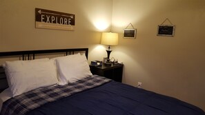 A neatly made bed with white and plaid bedding, a bedside lamp, a clock, and a wall sign that says "EXPLORE".