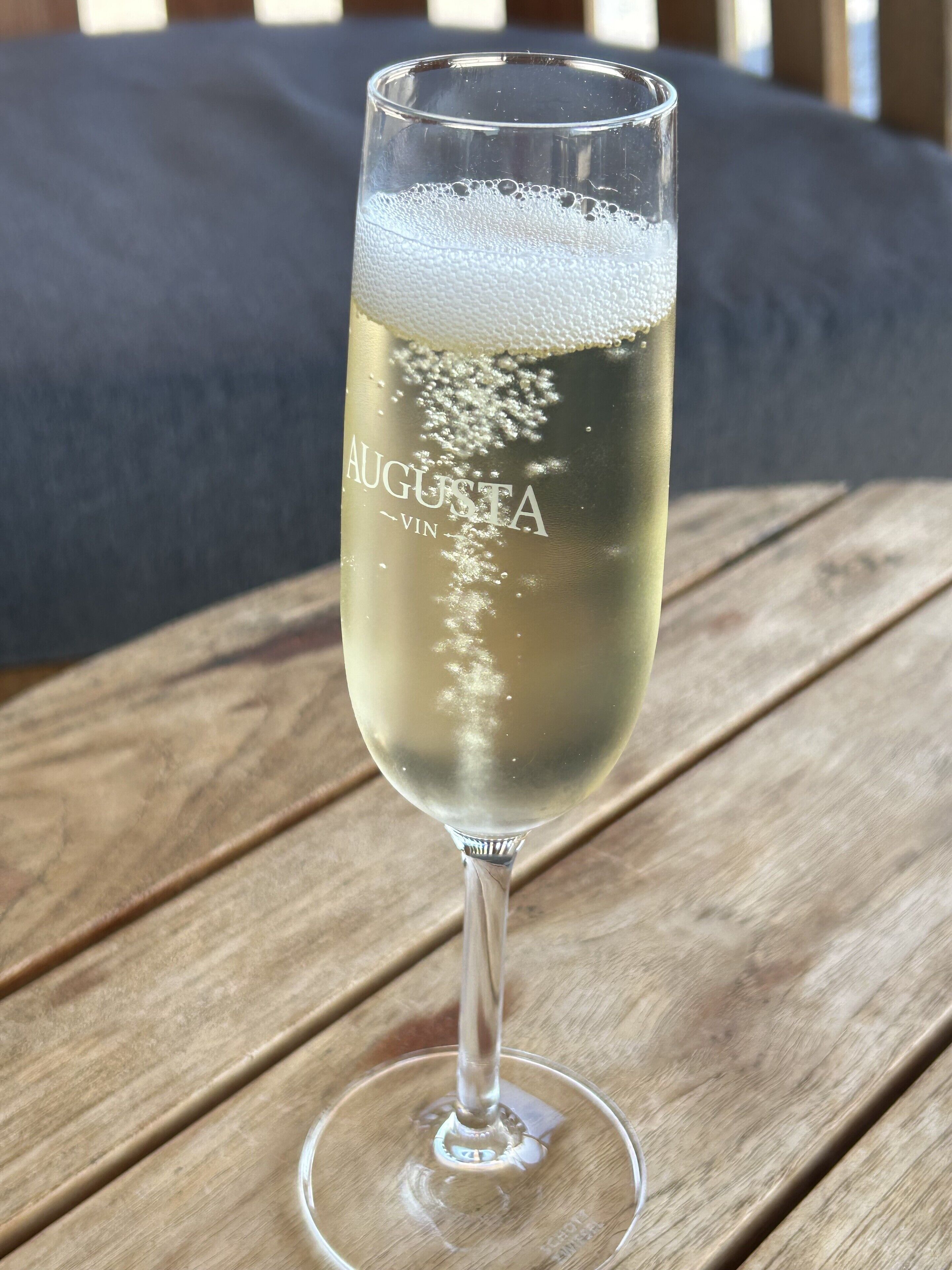 Ein Glas Sekt mit Bläschen auf einem Holztisch.