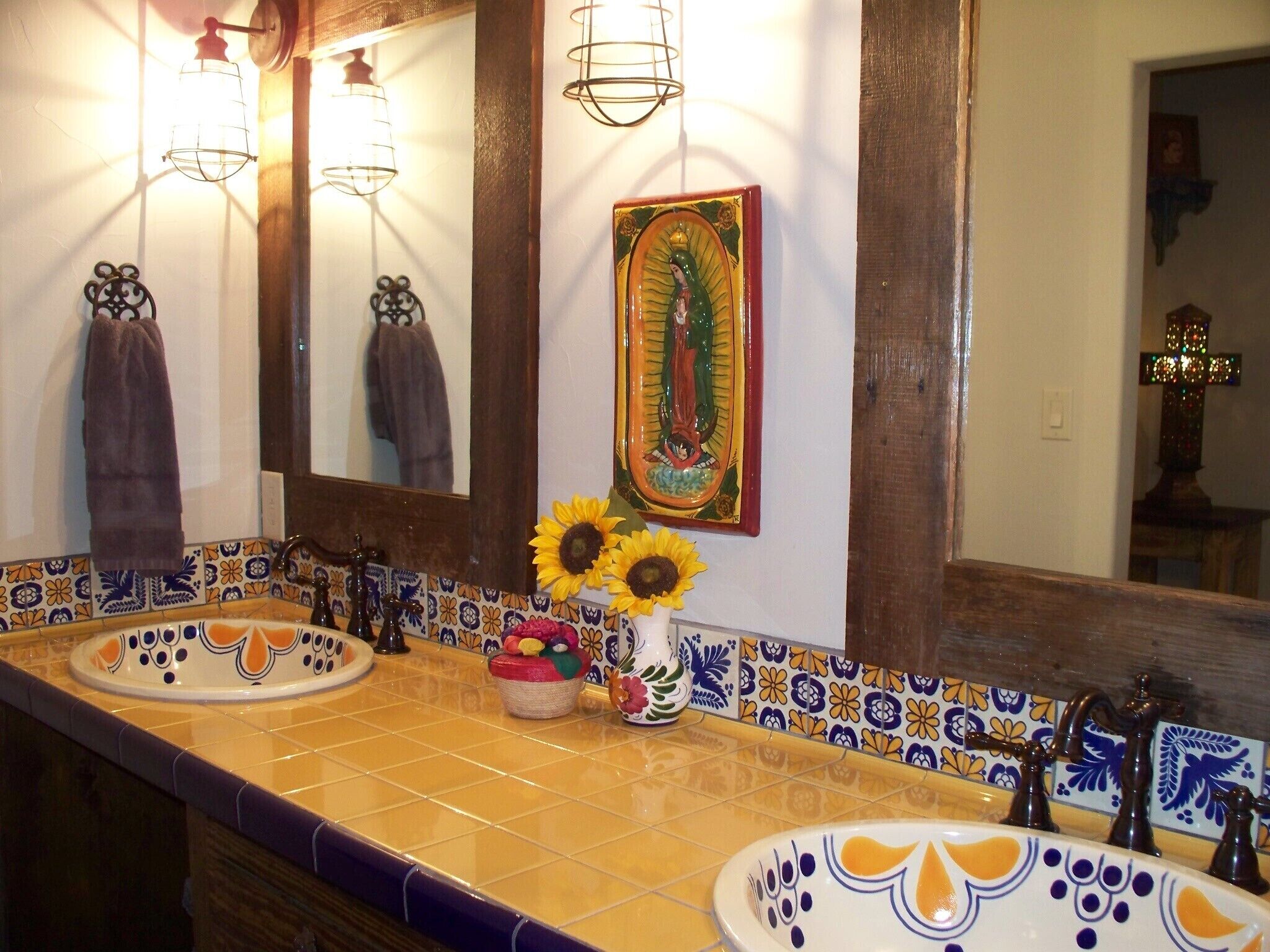 A bathroom with two sinks, a mirror, and a decorative wall with tiles and a religious painting.