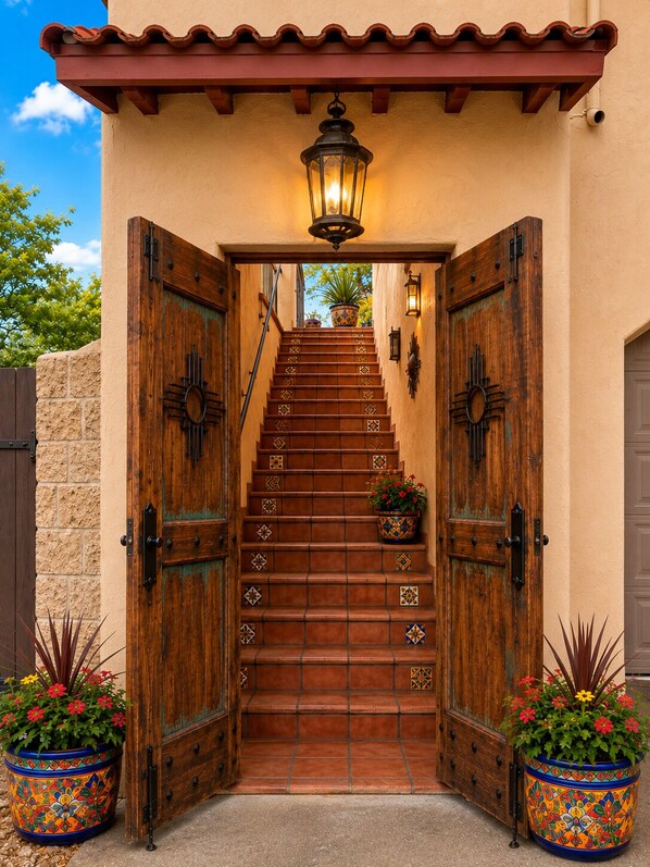 A set of wooden stairs leading to a door with a lantern above, flanked by two potted plants.