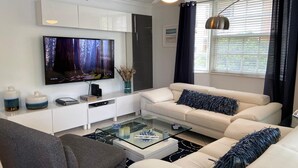 A modern living room with a flat-screen TV, white sofas, a glass coffee table, and a ceiling fan. - THE NAUTICAL!  FULLY EQUIPPED  3 BD 2BA APT AT AVENTURA  YACHT CLUB! (Aventura)