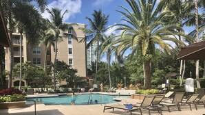A pool area with lounge chairs, palm trees, and a multi-story building in the background. - THE NAUTICAL!  FULLY EQUIPPED  3 BD 2BA APT AT AVENTURA  YACHT CLUB! (Aventura)