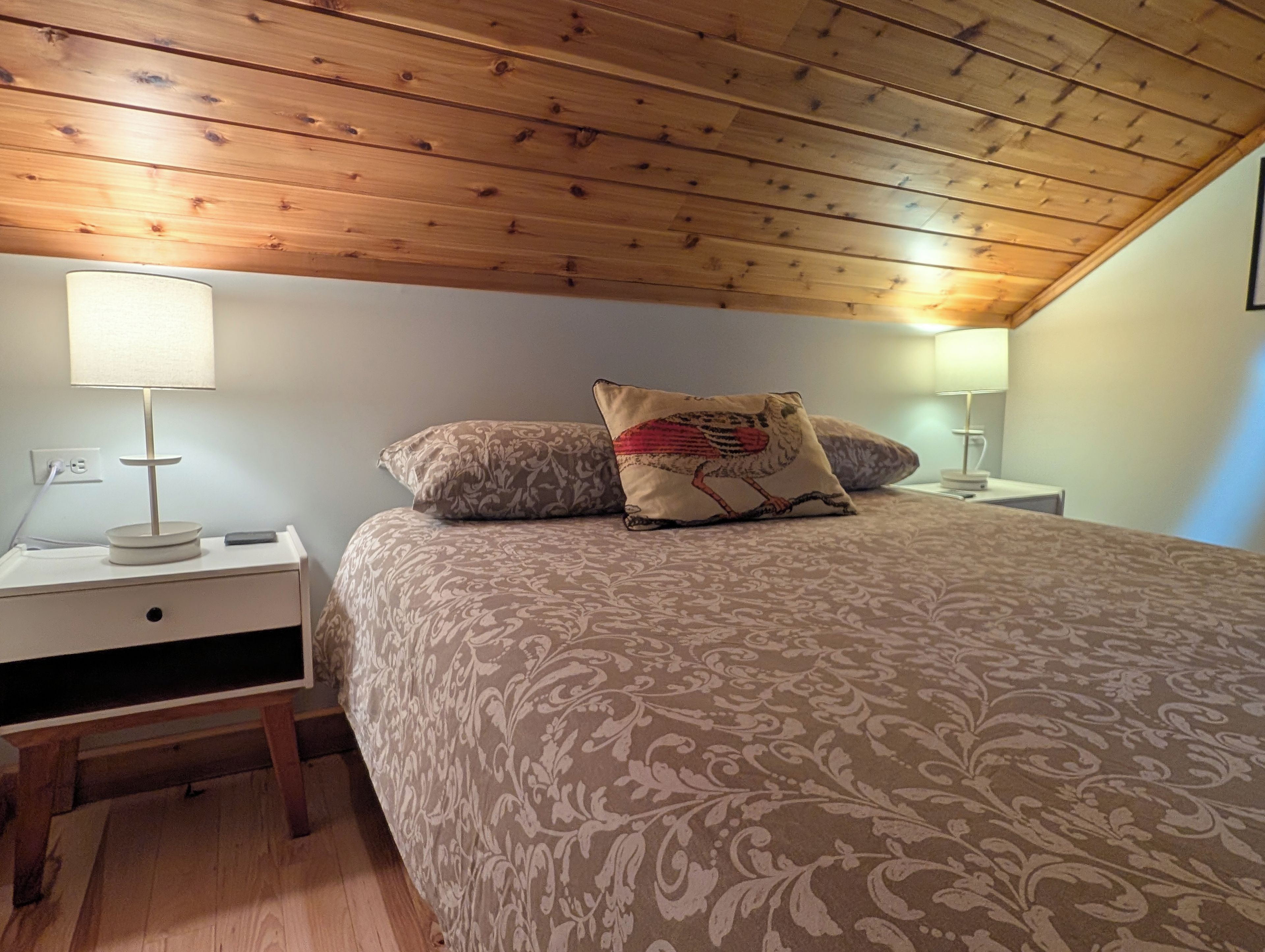Ein Schlafzimmer mit Holzboden, einem Bett mit gemusterten Bettwaren, zwei Nachttischlampen und einem Nachttisch mit Lampe.